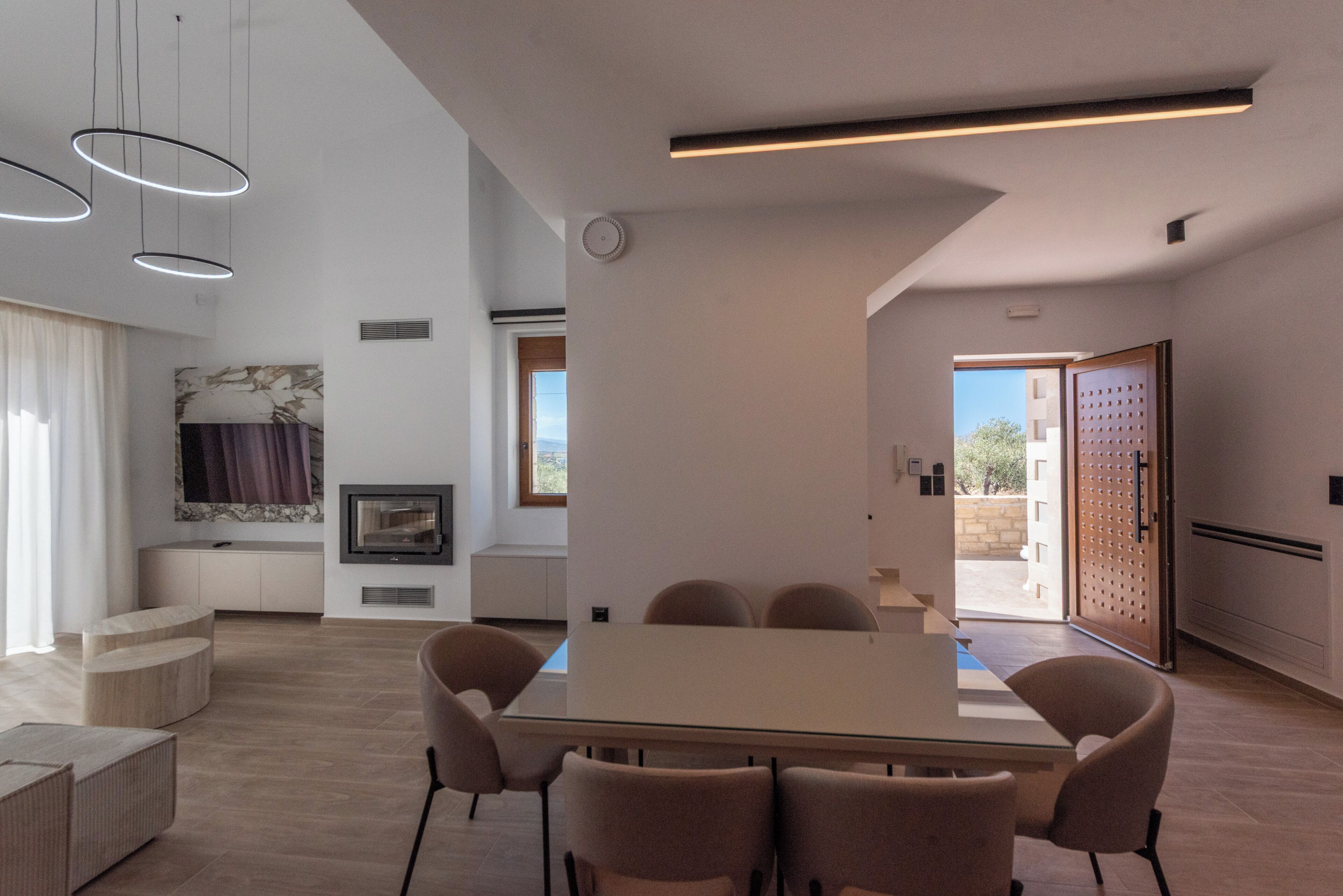 Un espace repas moderne avec une table en verre et six chaises, une cuisine intégrée et une grande fenêtre qui laisse entrer la lumière naturelle.