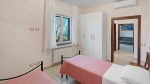 A room with two beds, a window with curtains, a radiator, a wardrobe, and an air conditioning unit. - Casa Vacanza Annì with Wi-Fi and Air Conditioning (Vico Equense)