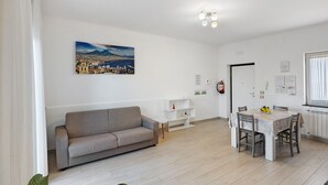 A modern living room with a sofa, a dining table with chairs, a painting on the wall, and a white door. - Casa Vacanza Annì with Wi-Fi and Air Conditioning (Vico Equense)