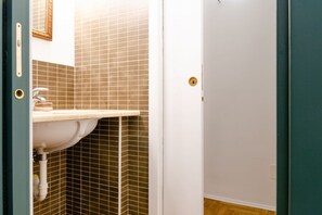 Une salle de bain avec un lavabo blanc, des murs carrelés et une porte dotée d’une poignée en laiton.