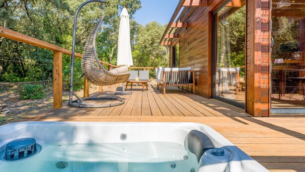 Eine Holzterrasse mit Whirlpool, Korbstühlen und einem Tisch mit Sonnenschirmen.