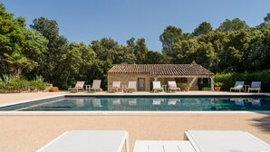 Ein Pool mit Liegestühlen, ein kleines Gebäude und Bäume im Hintergrund.