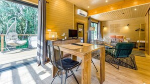Ein Holzinterieur mit einem Esstisch, Stühlen, einem Fernseher und einem Hängesessel neben einem großen Fenster.