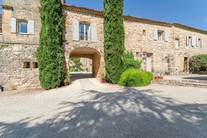 A stone building with a central archway, large potted plants, and a gravel driveway.