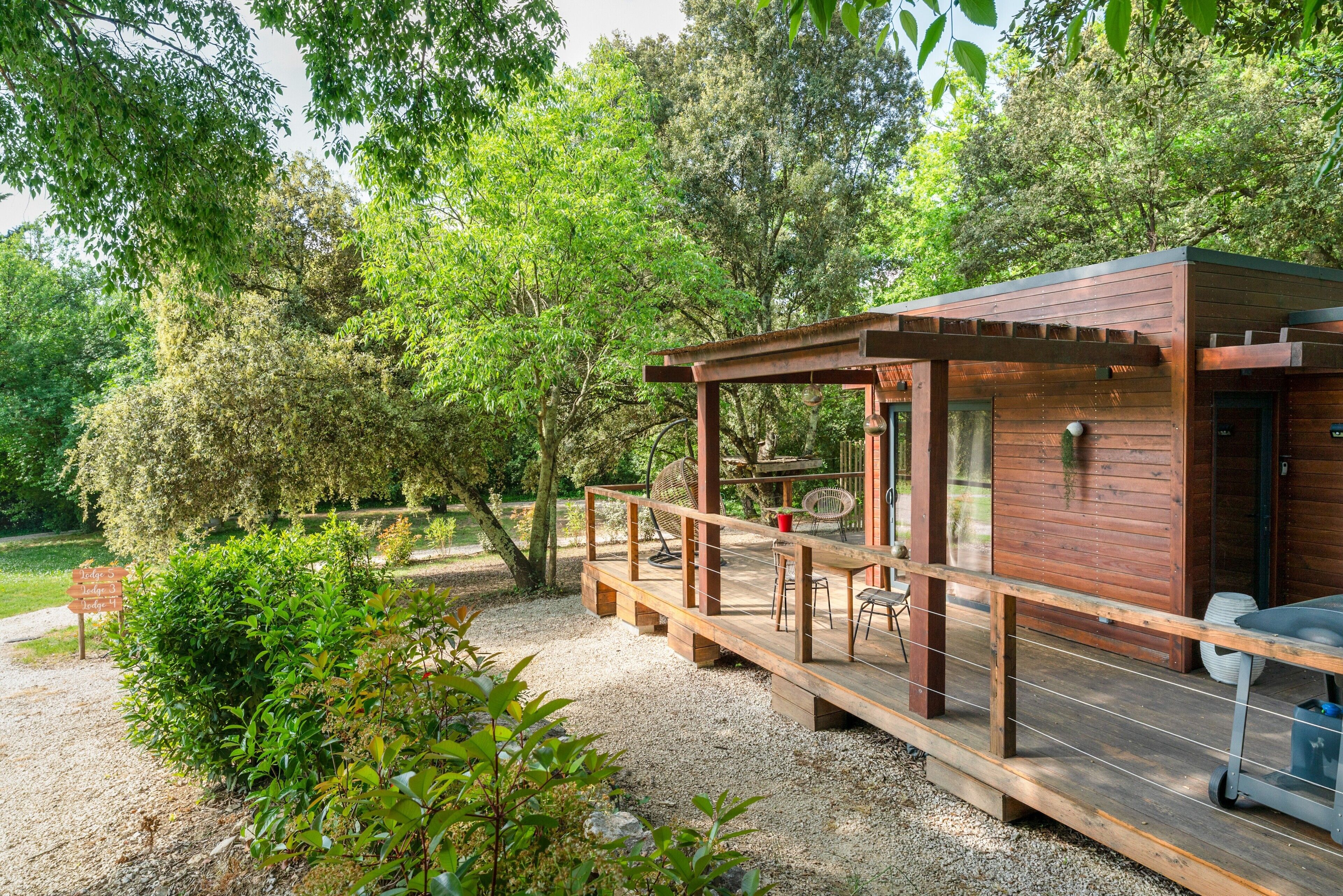 Une cabane en bois dotée d’une terrasse, entourée d’arbres et de verdure.