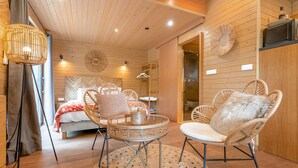 Una habitación acogedora con una cama, sillas de mimbre, una mesita redonda y una lámpara colgante.