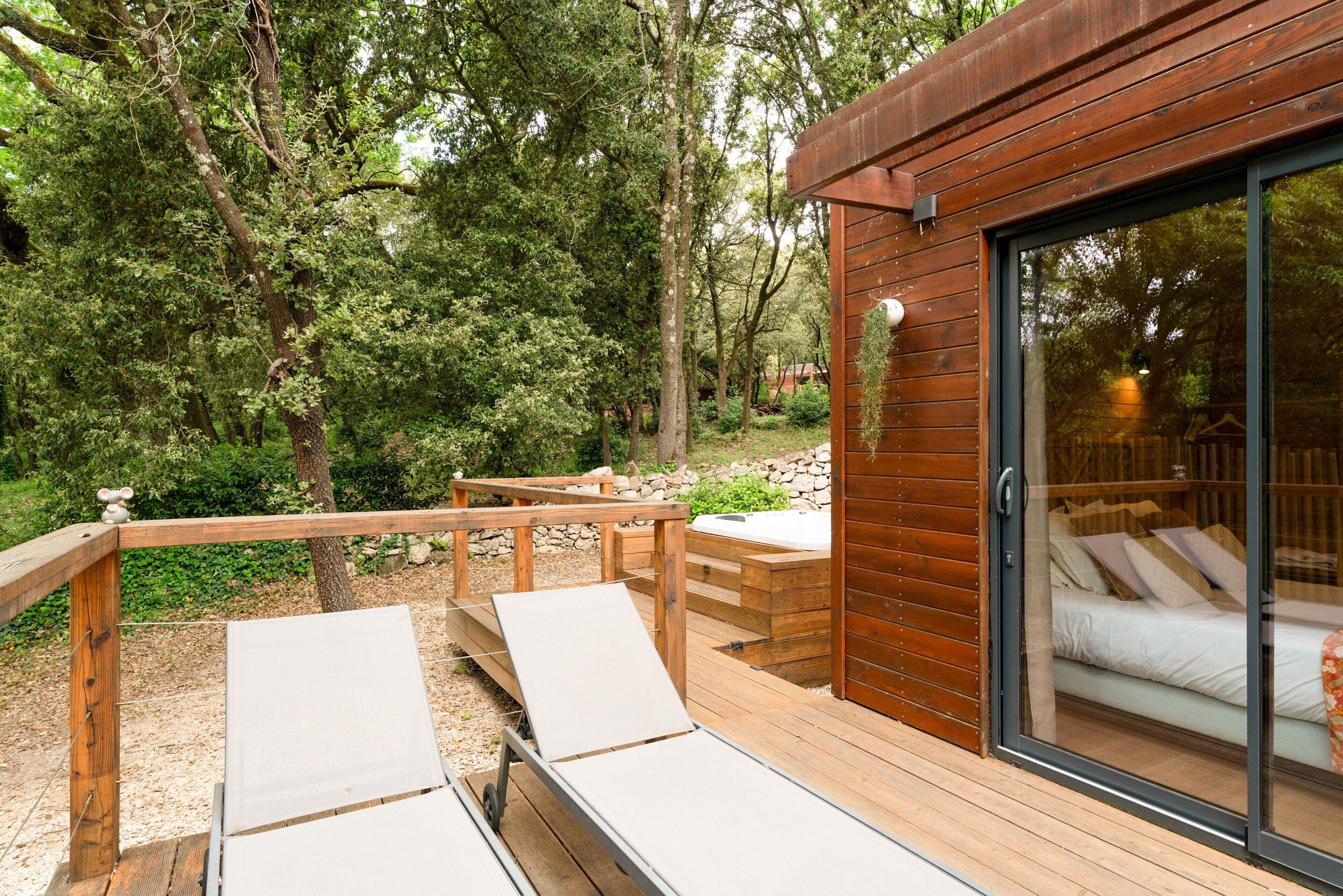 Une terrasse en bois avec deux chaises longues, un jacuzzi et une porte vitrée donnant sur une chambre à coucher avec un lit.