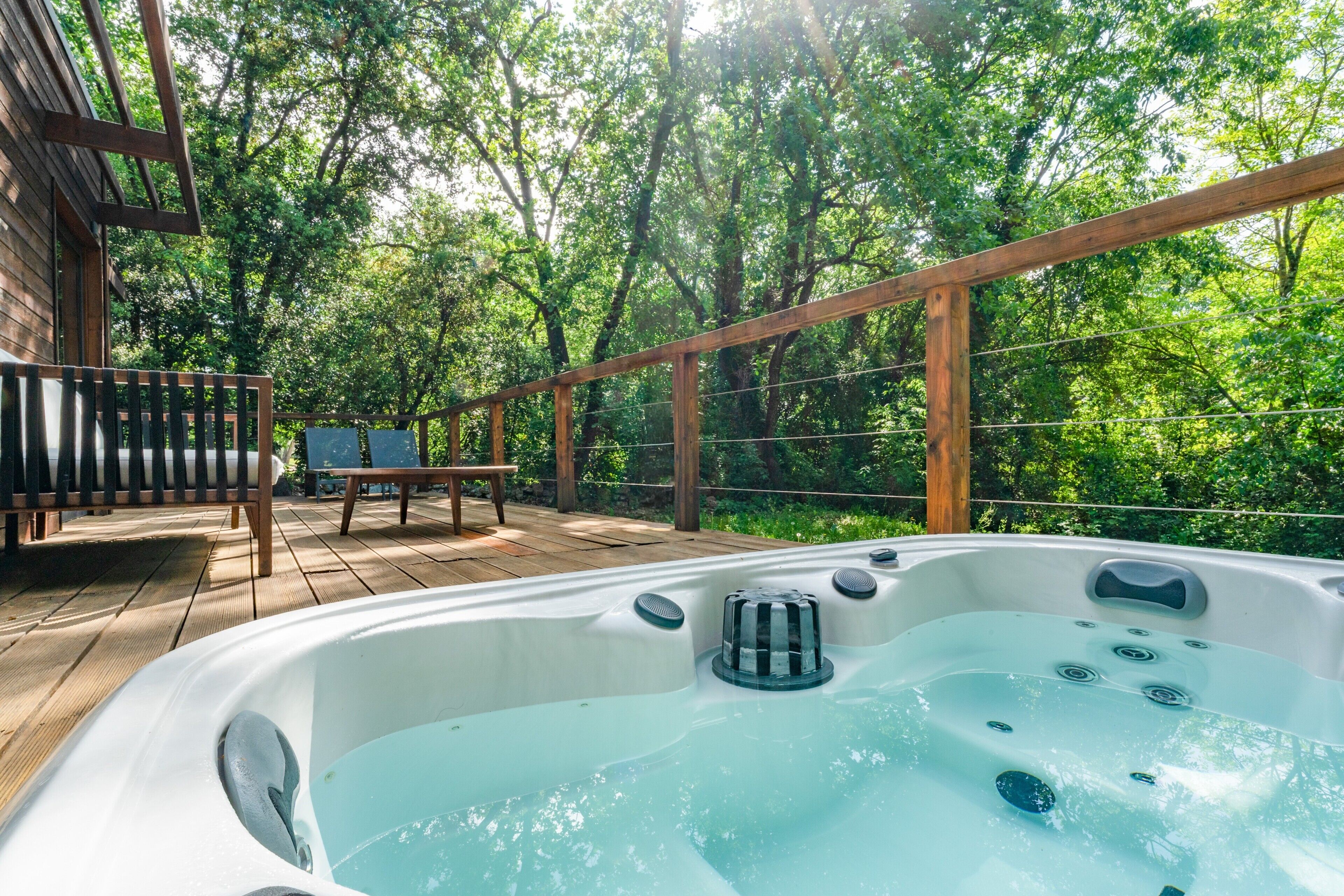 Een hottub op een houten terras met uitzicht op een bos.