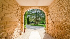 Un couloir voûté en pierre, avec un chemin de gravier menant à un jardin.