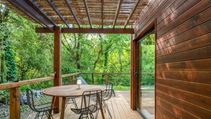 Une terrasse en bois, agrémentée d’une table et de chaises, entourée d’une balustrade en bois, et offrant une vue sur une zone boisée.