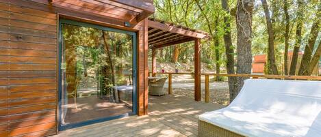 Eine Holzterrasse mit überdachter Sitzgruppe, einem Rattansofa und einer Glastür, die zu einem Außenbereich führt.