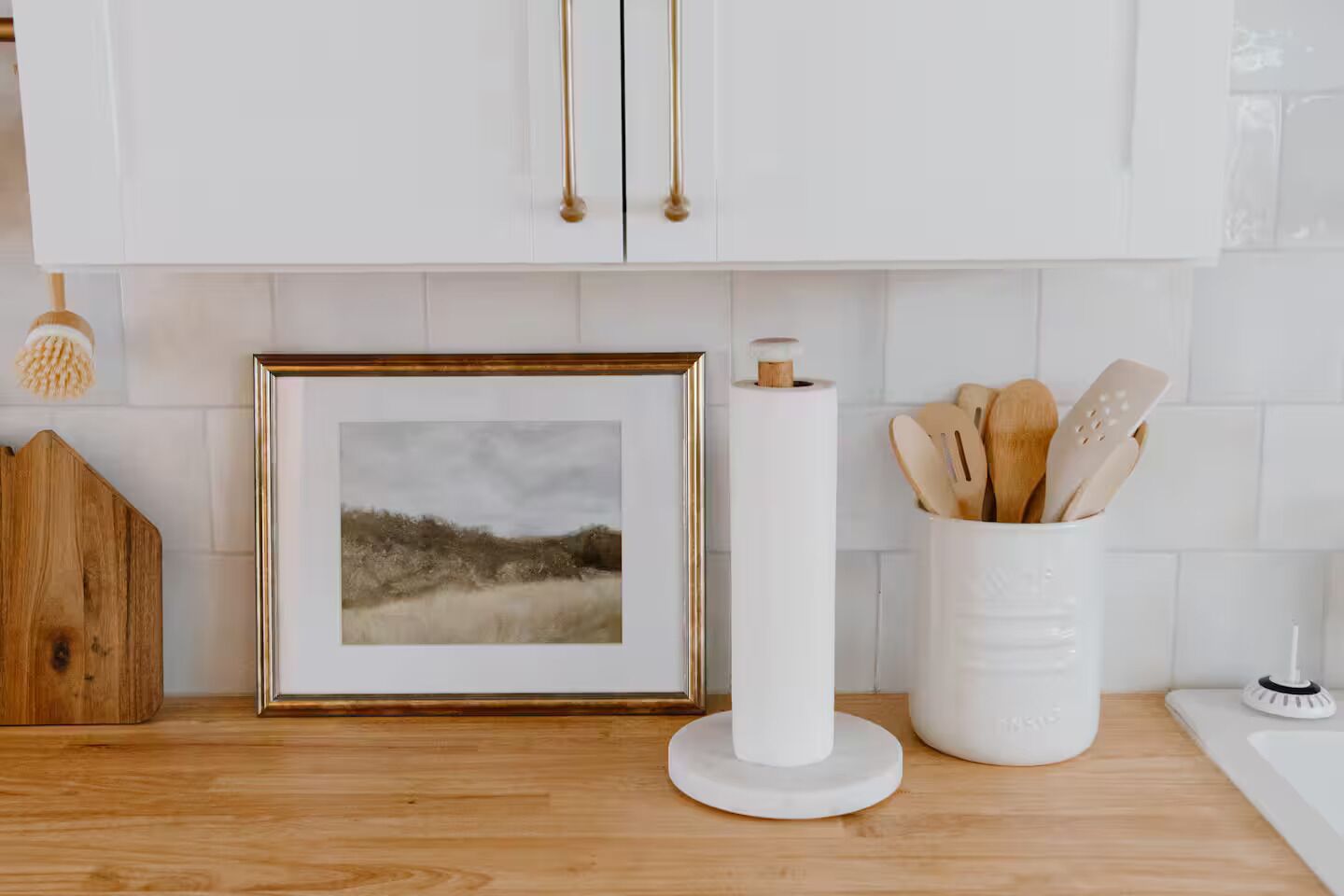 Cucina con mobili bianchi, una cornice appesa al muro, un candelabro bianco e utensili di legno in un contenitore.