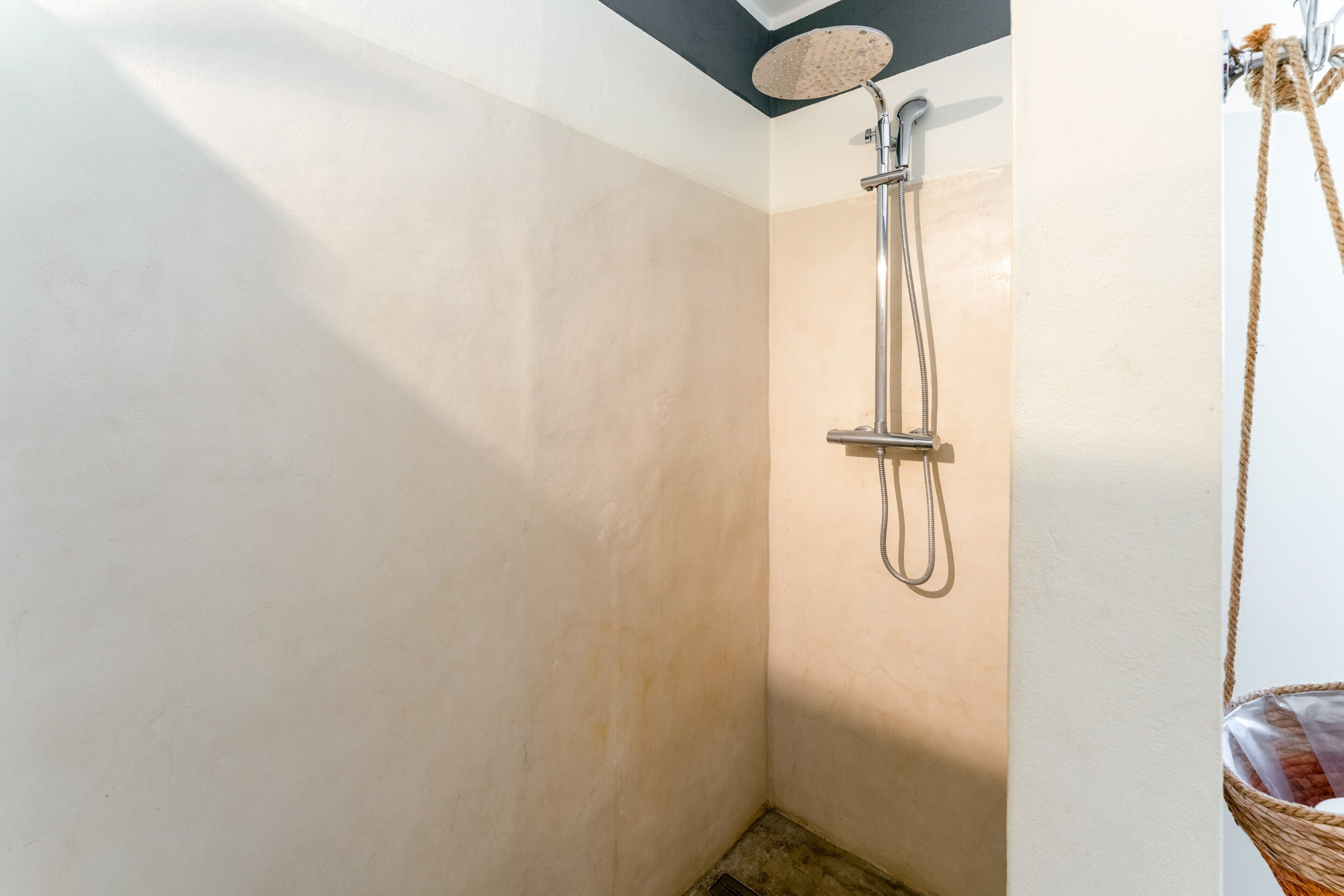 A shower with a handheld showerhead, a wall-mounted towel rack, and a corner with a woven basket.