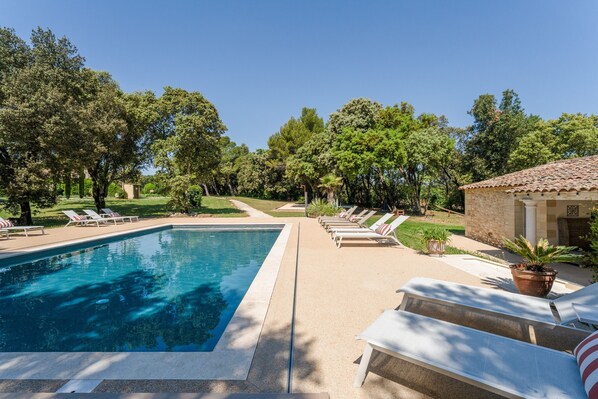 A swimming pool with lounge chairs, a stone building, and surrounding trees.
