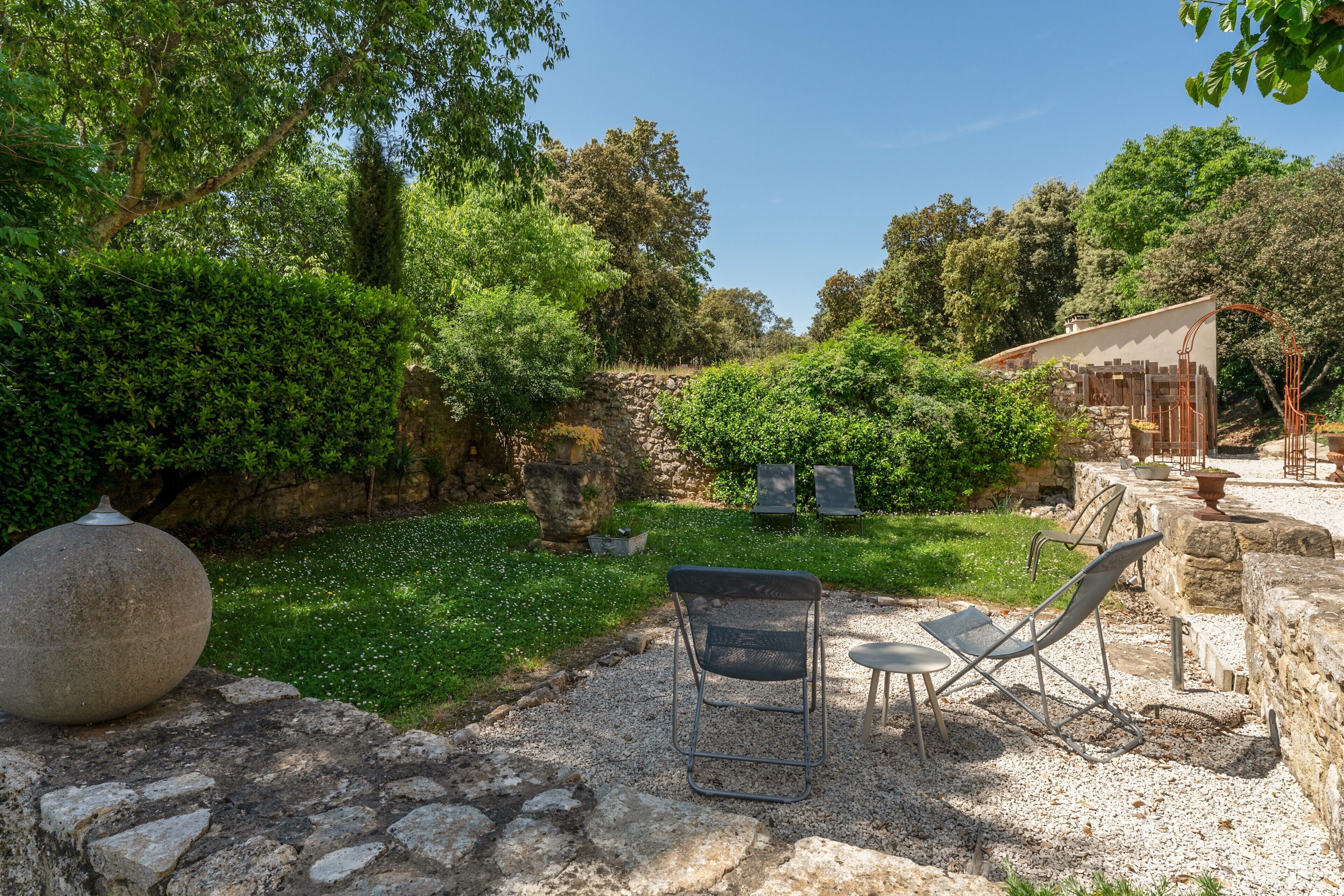 Un espace jardin aménagé avec des bancs en pierre, une pergola et un mur en pierre.