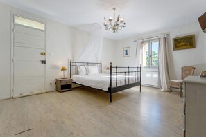 Een slaapkamer met een bed, nachtkastje, lamp, raam met gordijnen en een schilderij aan de muur.