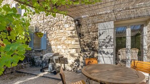 Une terrasse extérieure avec un mur en pierre, une table avec des chaises et un barbecue.