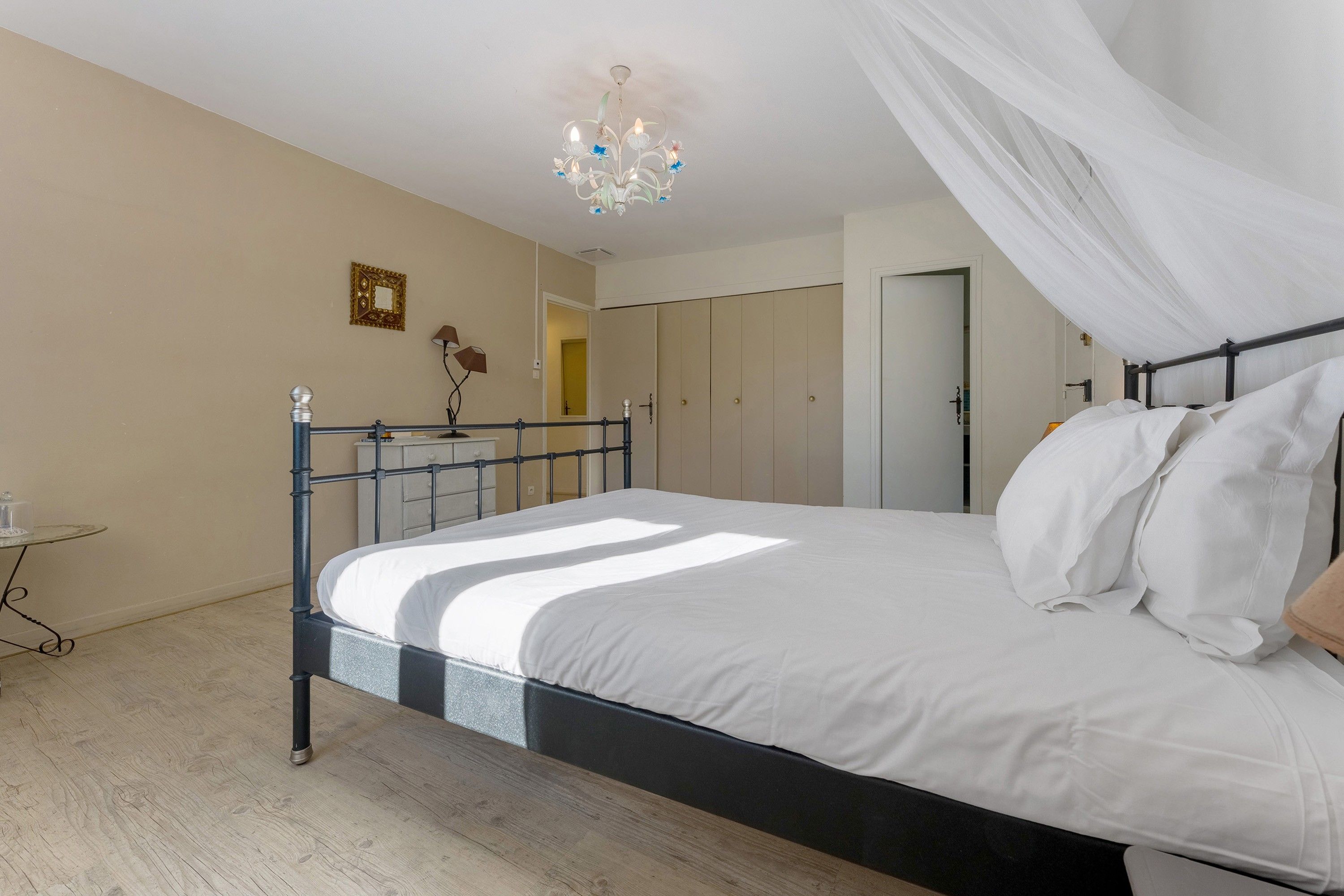 Een slaapkamer met een bed, een nachtkastje, een lamp, een spiegel en een kroonluchter.