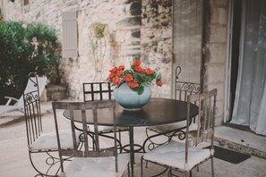 Une table ronde surmontée d’un vase bleu contenant des fleurs rouges, entourée de quatre chaises dotées de coussins blancs.