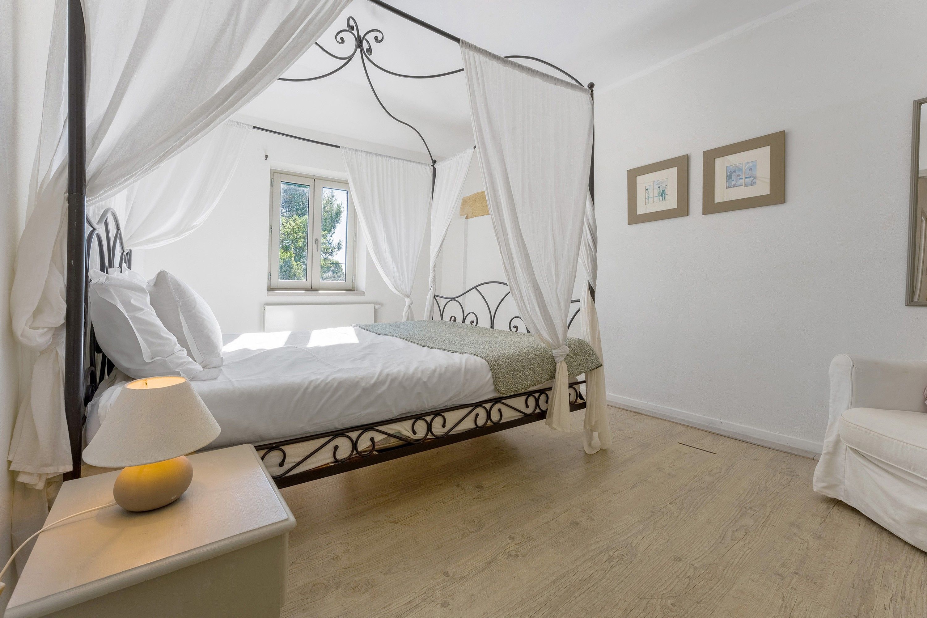 Una camera da letto con un letto a baldacchino, un comodino con una lampada, una finestra con tende e una parete decorata con quadri.