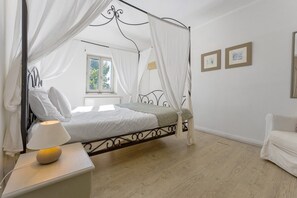 Une chambre à coucher avec un lit à baldaquin, une table de chevet avec une lampe, une fenêtre avec des rideaux et un mur orné de tableaux.