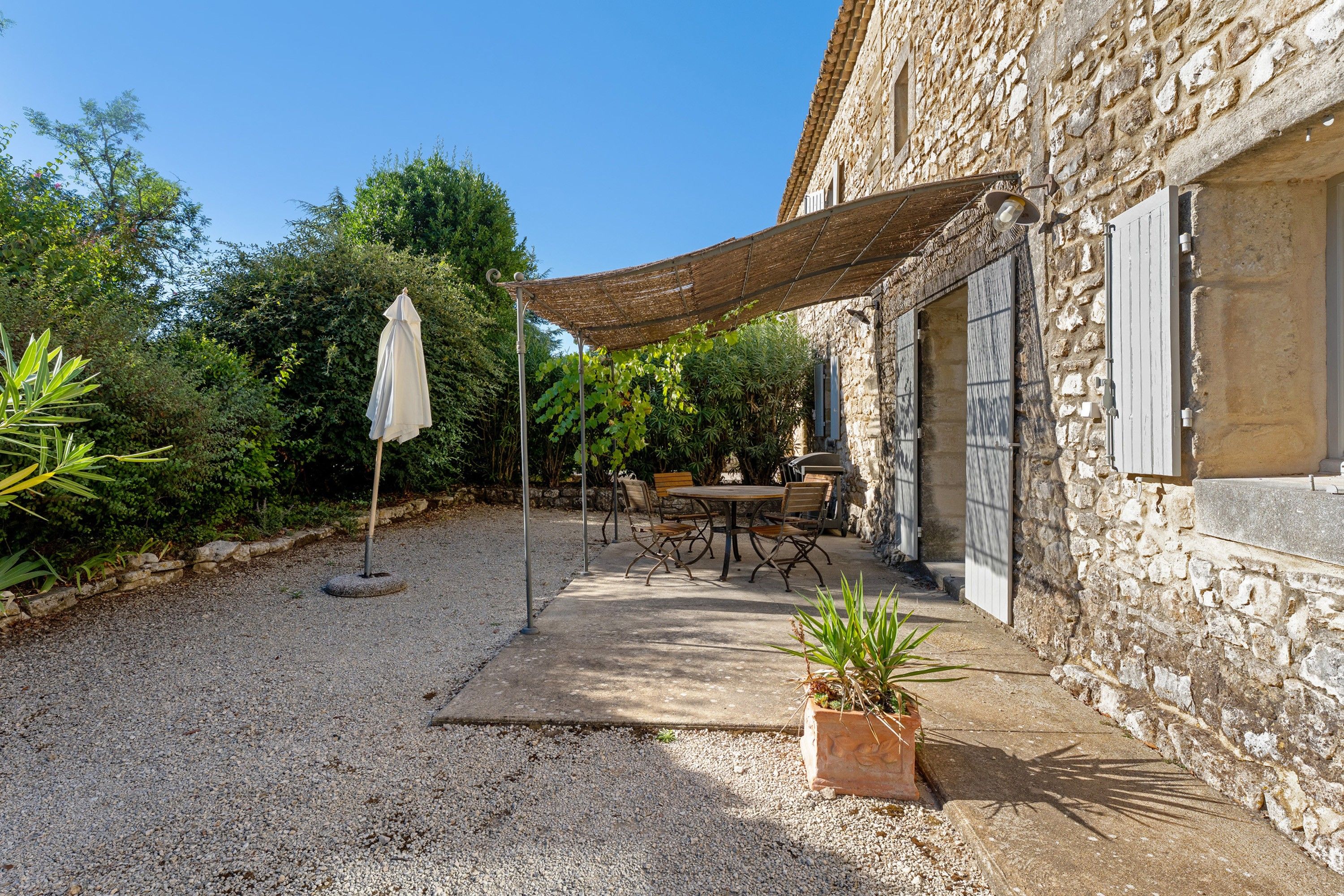 Un edificio in pietra con un patio lastricato di ghiaia, mobili da esterno e una zona ombreggiata.