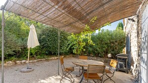 Une terrasse extérieure avec une table ronde et des chaises, une pergola au-dessus et un espace barbecue.