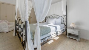 Un lit à baldaquin avec des rideaux blancs, une table de chevet avec une lampe et une petite commode.
