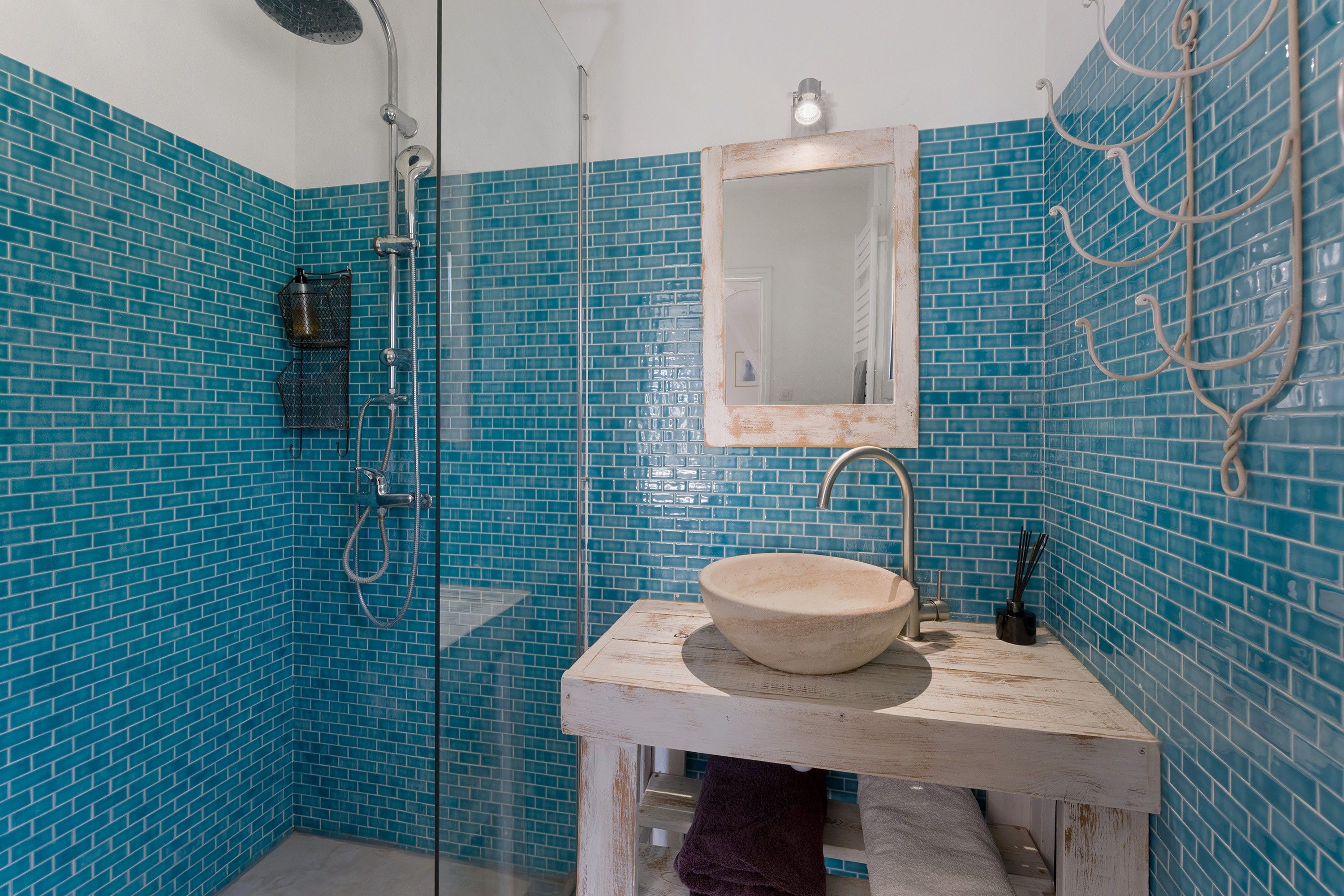 Ein Badezimmer mit einer Duschkabine, einem Waschbecken mit Spiegel darüber und blauen Fliesen.