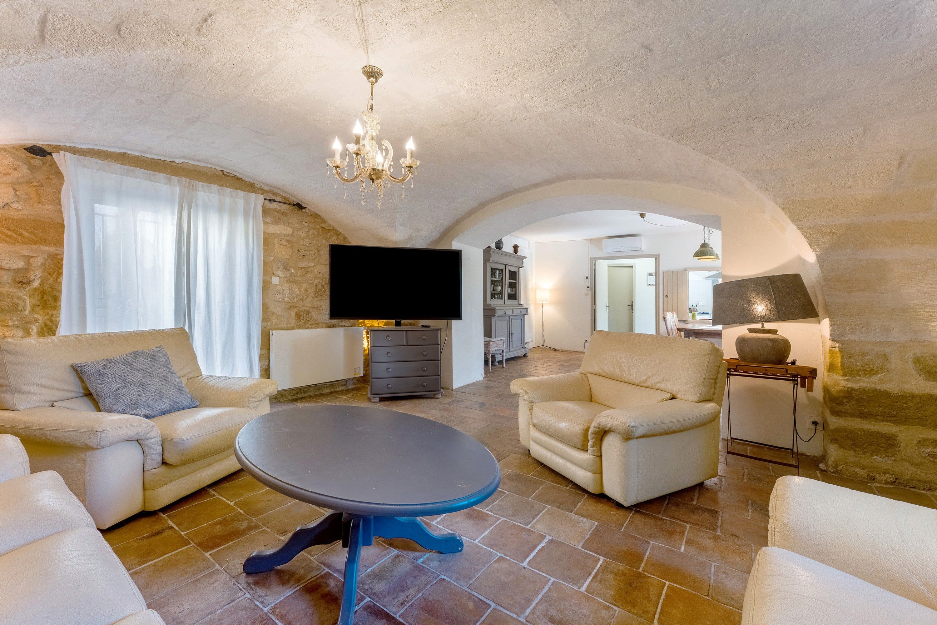 A spacious living room with a stone wall, a chandelier, a flat-screen TV, and leather sofas.