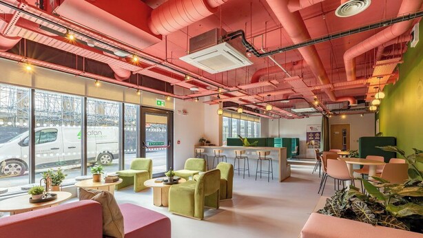 A modern interior with green seating, a bar area, and large windows overlooking a street. - Student Only The Brook (Bath)
