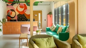 A modern lounge area with a green sofa, two armchairs, a small table, and a colorful abstract wall art. - Student Only The Brook (Bath)