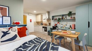 A modern, compact living space with a kitchenette, a dining area, and a bedroom. - Student Only The Brook (Bath)