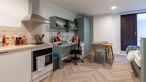 A compact kitchen with modern appliances, a dining area with a wooden table, and a bed with a view. - Student Only The Brook (Bath)