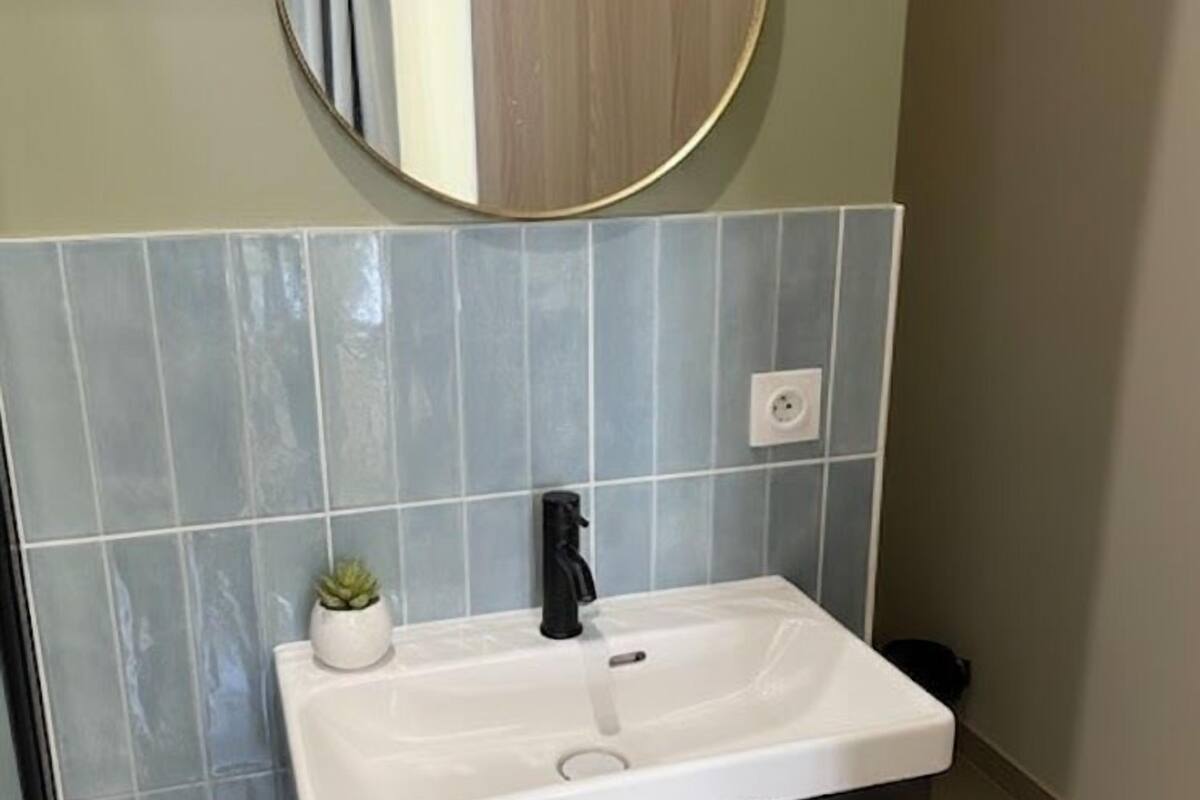 A bathroom with a round mirror, a white sink, a small potted plant, and a towel hanging on a cabinet.