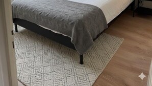 Un dormitorio con cama, mesita de noche, lámpara, un cuadro enmarcado en la pared y una ventana con cortinas.