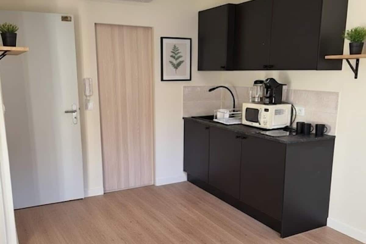 A compact kitchen with dark cabinets, a microwave, a kettle, and a small countertop.