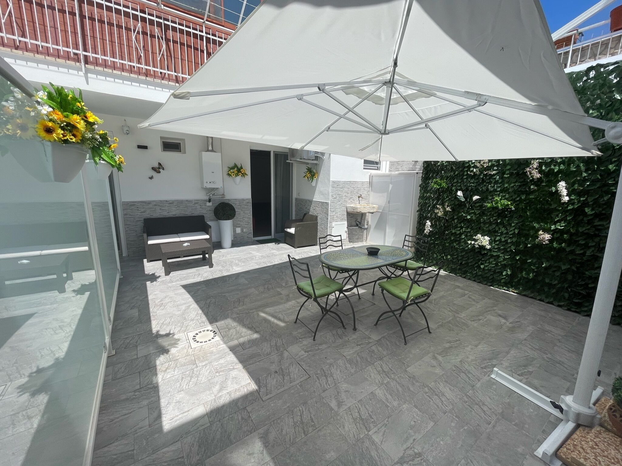 Un espace patio aménagé avec une table et des chaises, un parasol blanc et un mur végétal orné de plantes grimpantes.