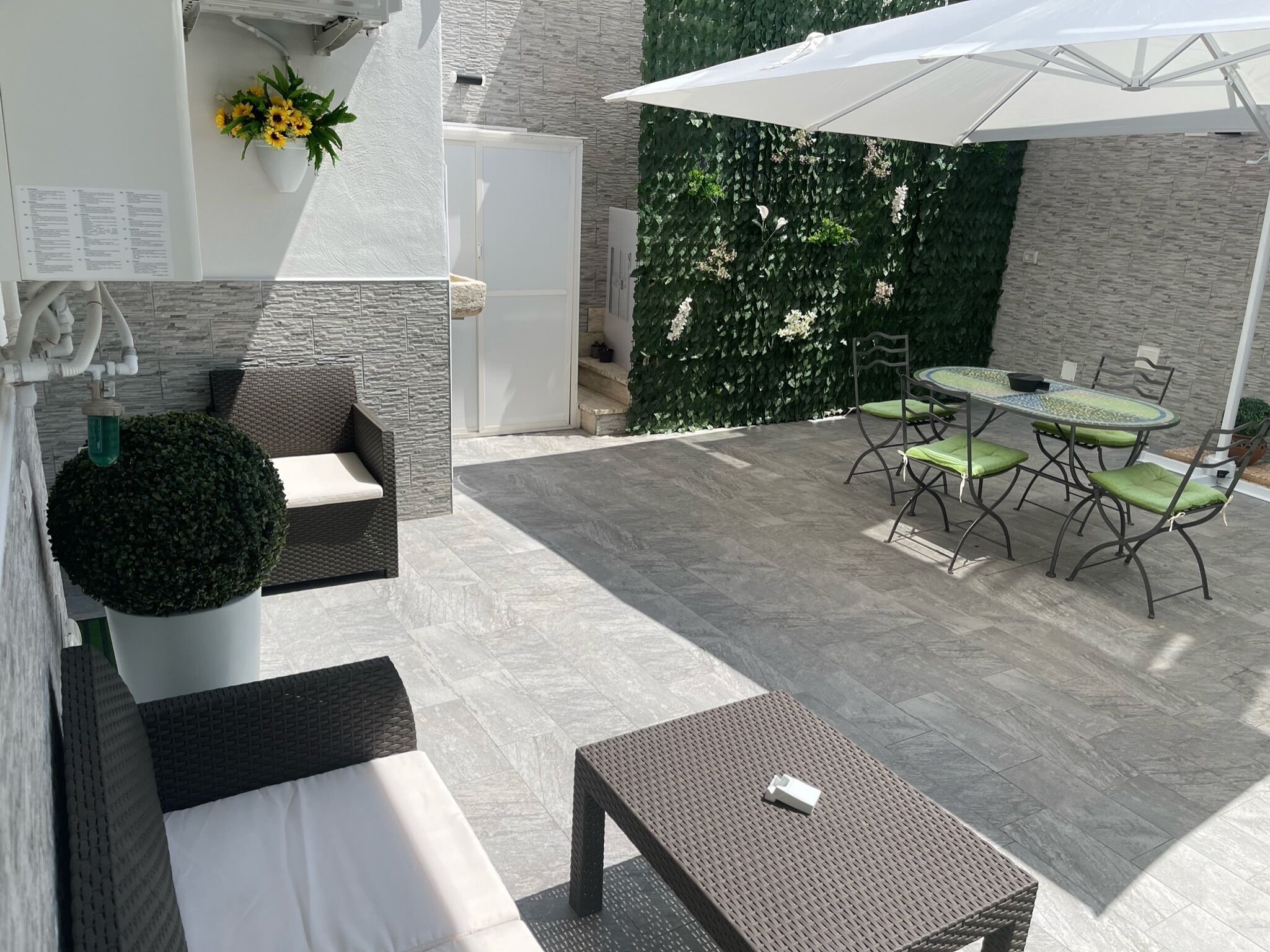 Un patio moderno al aire libre con comedor, asientos y una pared decorativa.