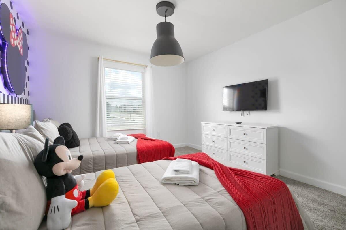 Una camera d'albergo con due letti, una TV, un comò e un pupazzo di Topolino.