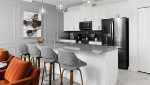 Una cocina moderna con armarios blancos, un refrigerador de acero inoxidable y una barra con sillas grises.