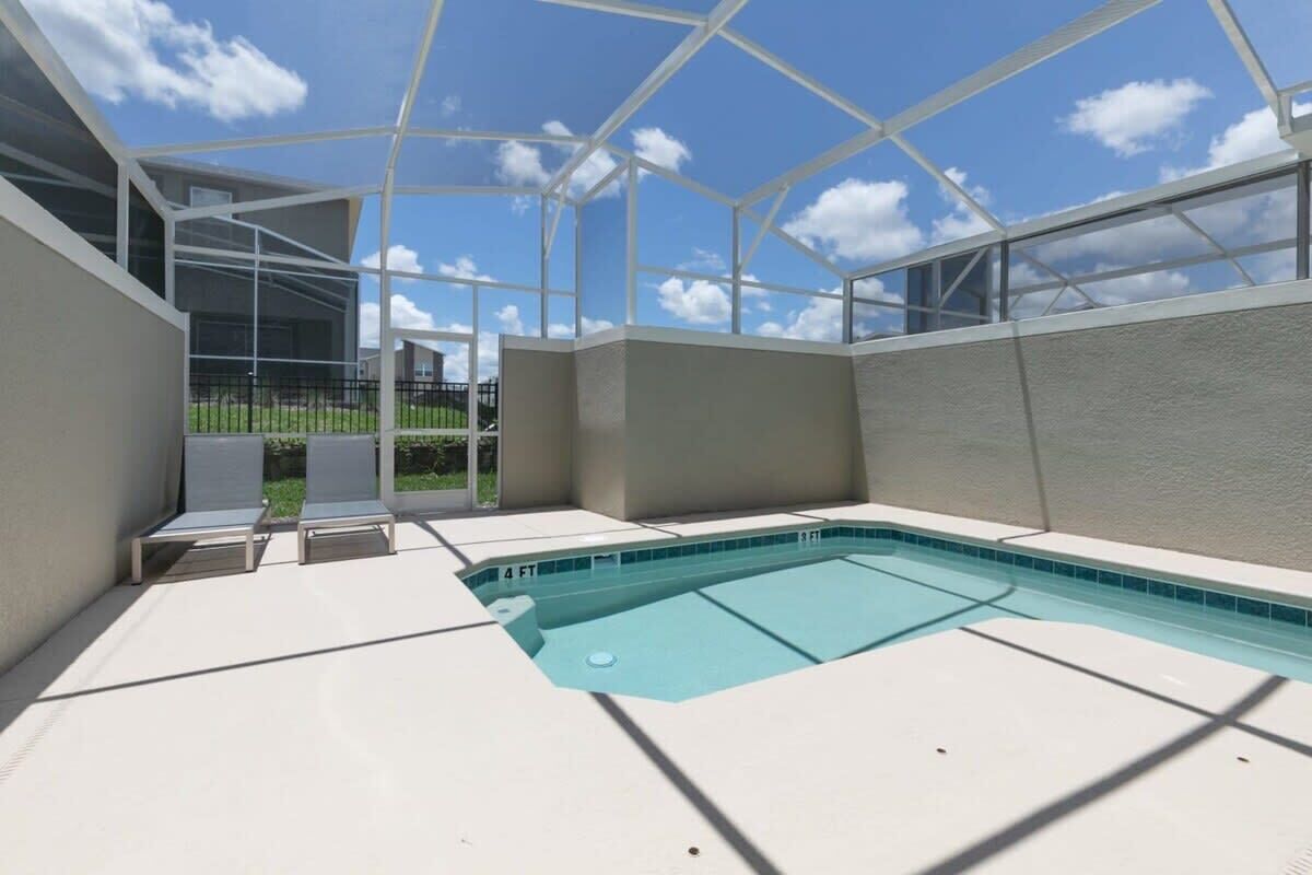 A swimming pool with a glass enclosure, lounge chairs, and a clear view of the sky.