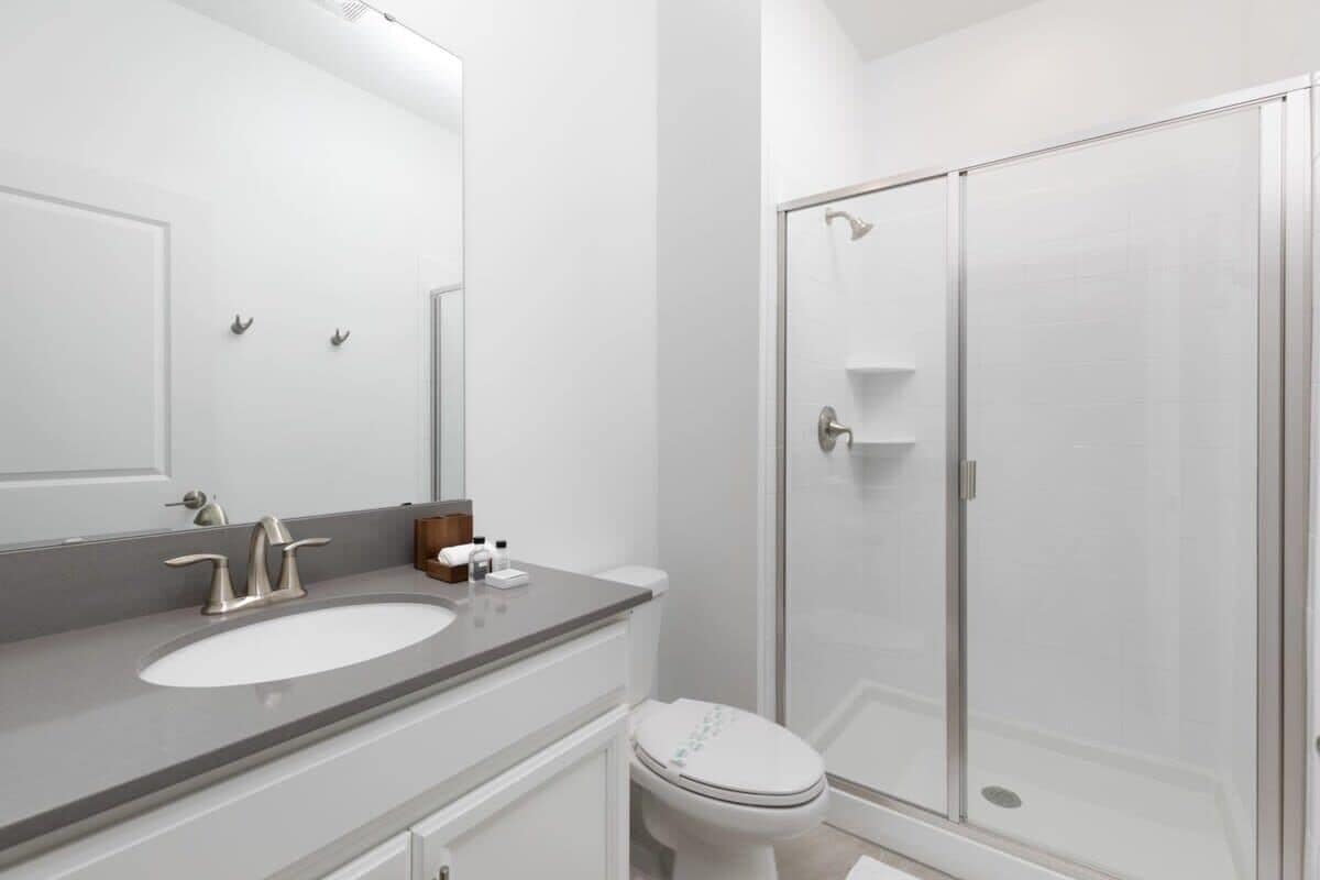 Un baño moderno con lavamanos, espejo, inodoro y cabina de ducha con paredes de vidrio.