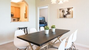 Un coin repas avec une table en bois foncé, des chaises blanches et deux plantes en pot.