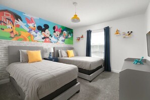 Un dormitorio con dos camas, un mural de personajes de Disney, un escritorio y una ventana con cortinas.