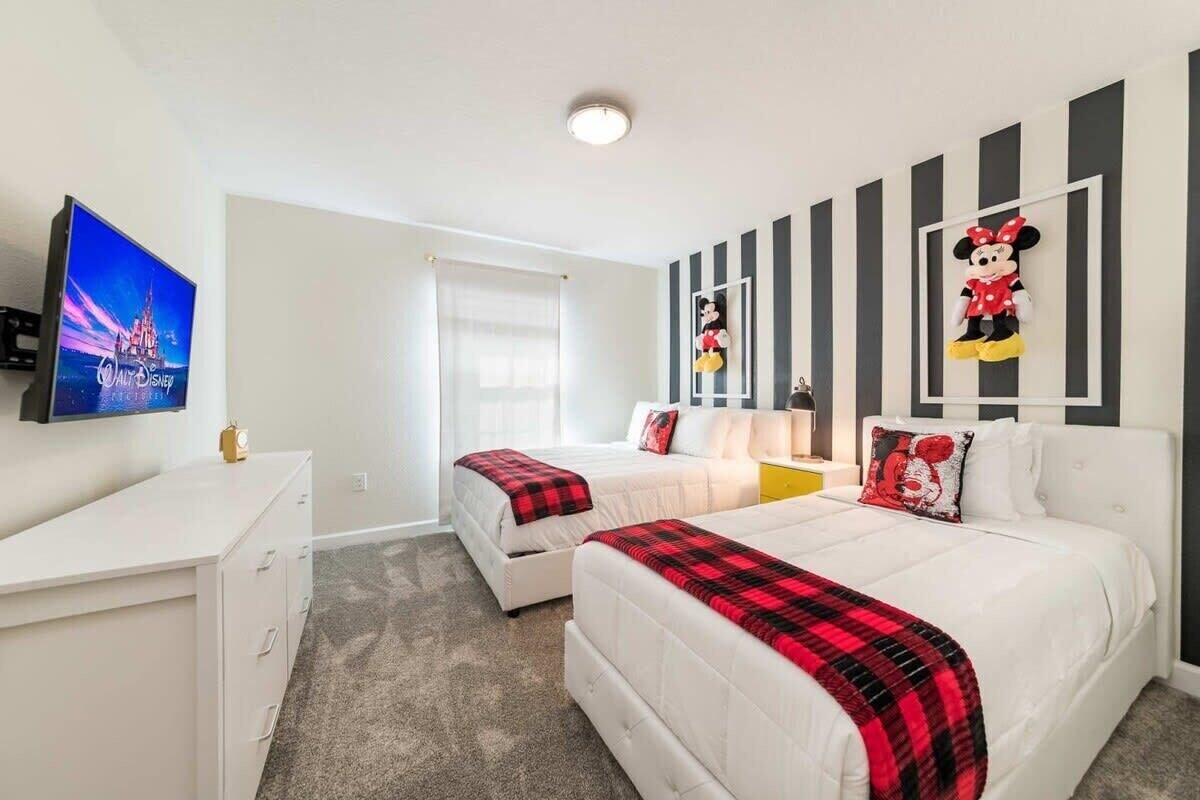 A hotel room with two beds, a TV, a desk, and a Mickey Mouse decoration on the wall.