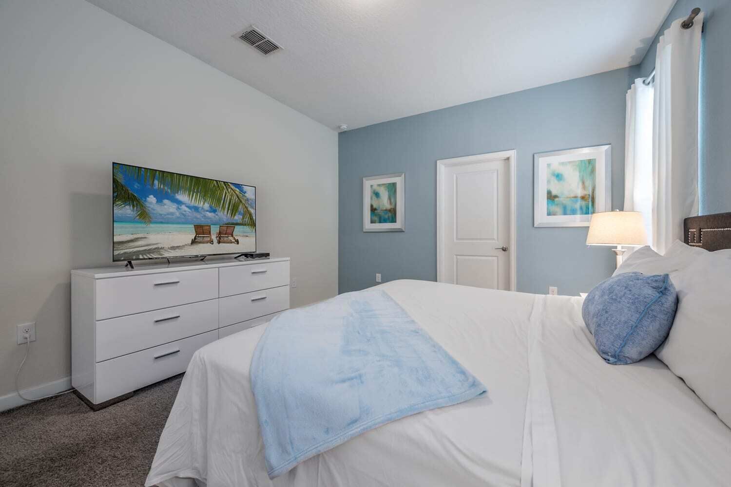 A bedroom with a bed, a dresser, a television on the dresser, and two doors.