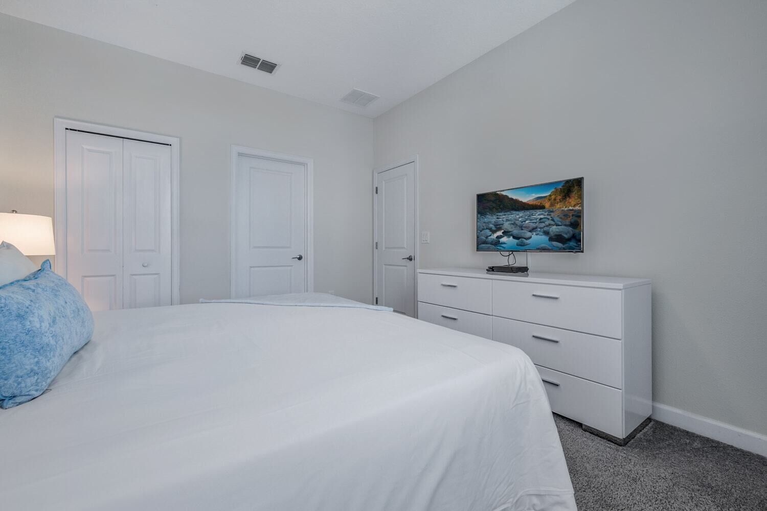 A bedroom with a bed, a dresser, a television, and two doors.