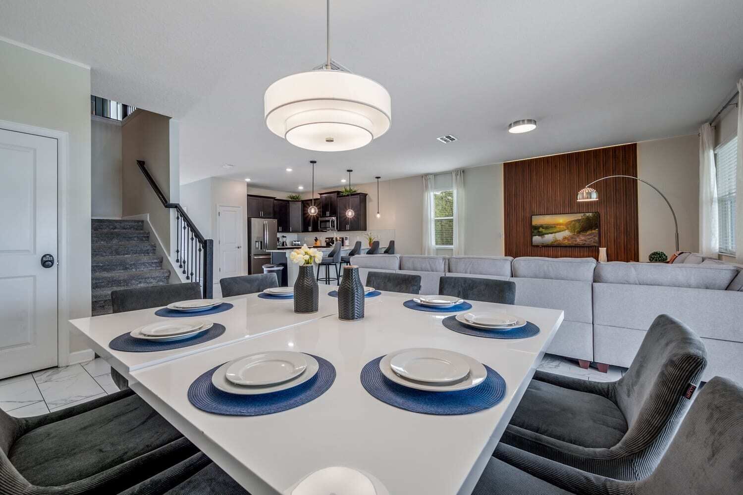 Uma sala de jantar moderna com uma mesa branca, cadeiras escuras e uma luminária central.