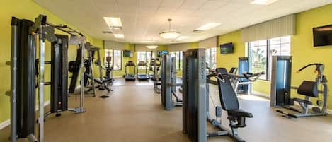 A gym with various exercise machines, a television, and large windows.